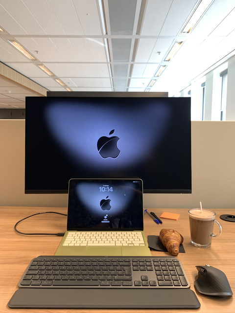A desk with a monitor, tablet, keyboard, coffee and pastry