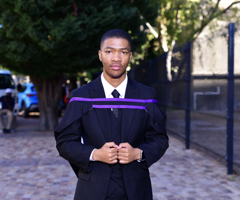Iviwe in a suit and graduation gown outdoors